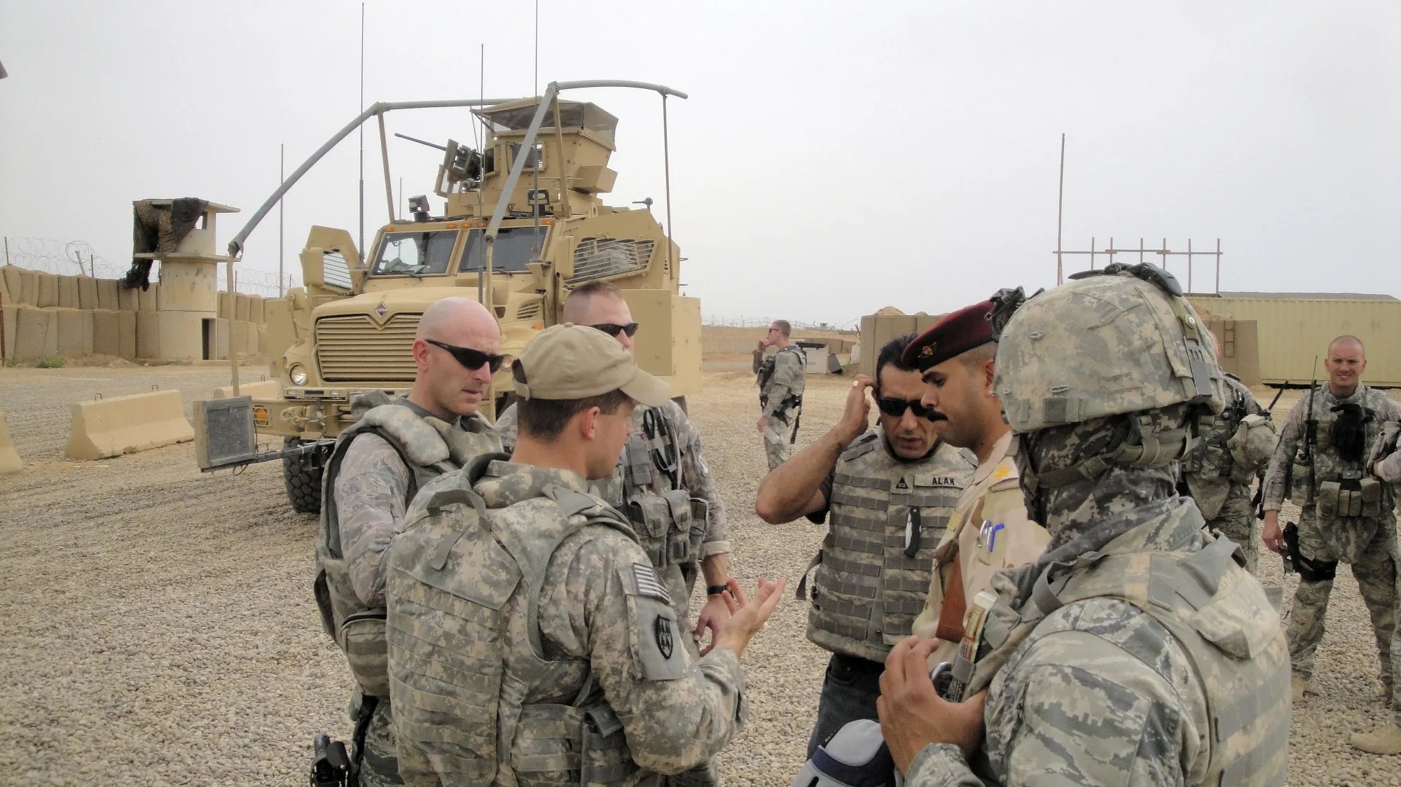 Service members gathered beside an armored vehicle at a desert outpost