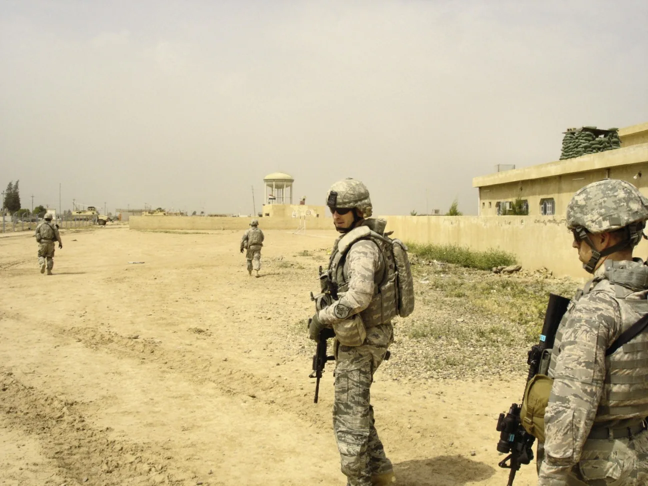 Soldiers on foot patrol along a dirt road under an open sky
