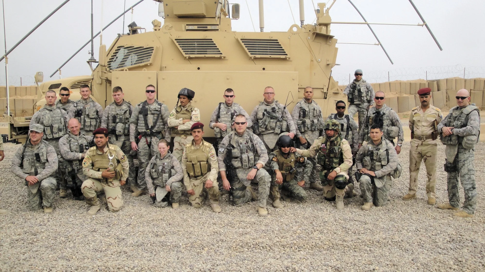 Group photograph of a deployed unit assembled in front of an armored vehicle